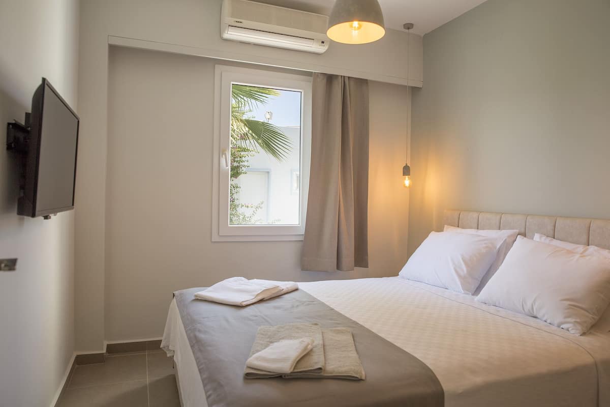 A hotel room with a bed, a TV mounted on the wall, a window with curtains, and a ceiling fan.