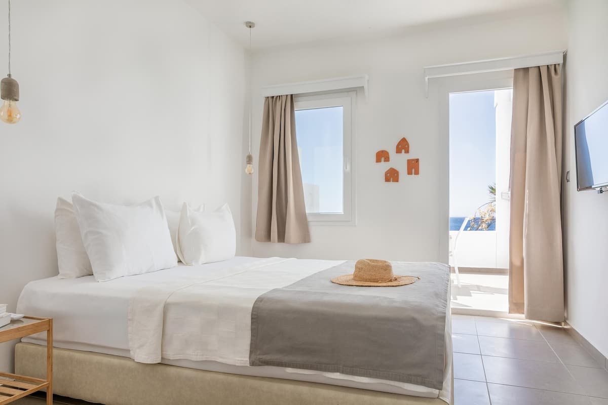 A bedroom with a bed, a TV, a window, and a view of the outside.