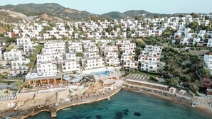 An aerial view of a coastal town with white buildings, a beach, and a pool area. - YAZ Yalikavak (Bodrum)