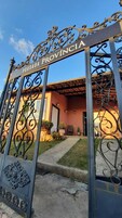 Una reja de hierro forjado con la inscripción 'POUSADA PROVINCIA' que da acceso a un edificio con techo de tejas y una entrada visible.