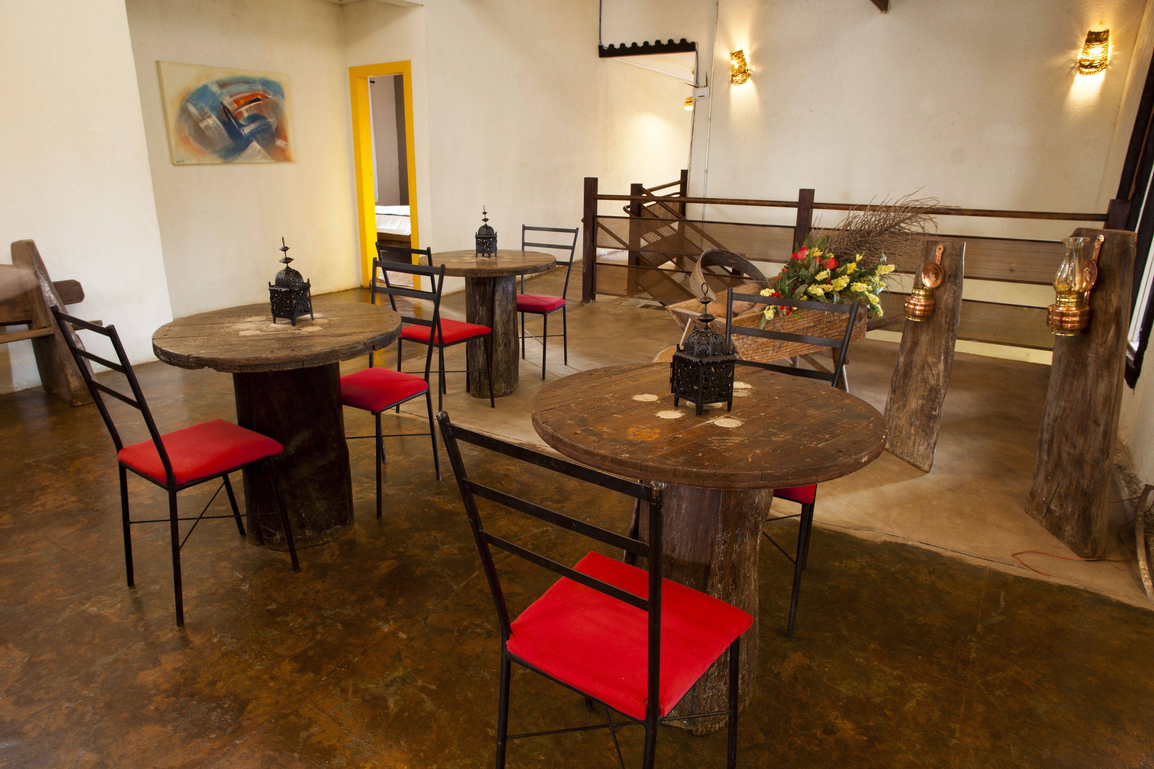 A restaurant with round wooden tables and red cushioned chairs. There are decorative lanterns on the tables, and a wooden bench in the background.
