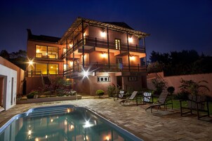 Un edificio de dos pisos con piscina, asientos al aire libre y un balcón bien iluminado.