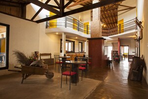 Un interior espacioso con techo alto, vigas de madera, una zona de comedor central con sillas rojas y un carrito de madera rústico.