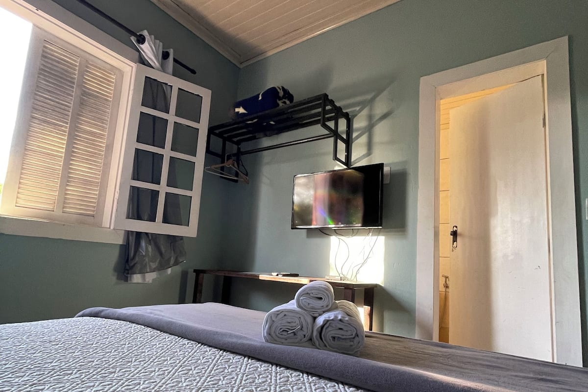 Une chambre à coucher avec un lit, une télévision, une fenêtre avec des stores et une porte.