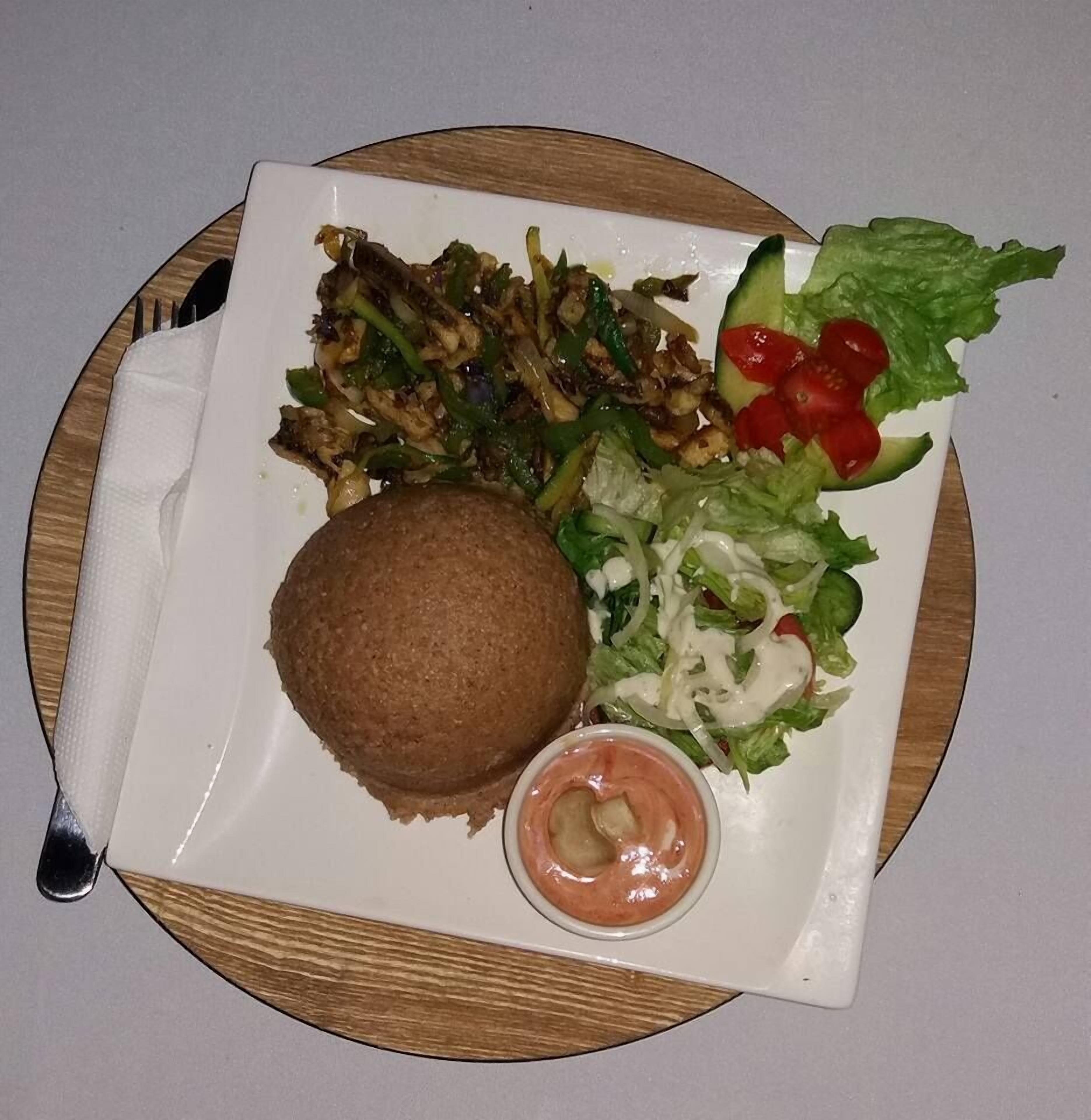 A plate with a burger, a side salad, and a small container of sauce.