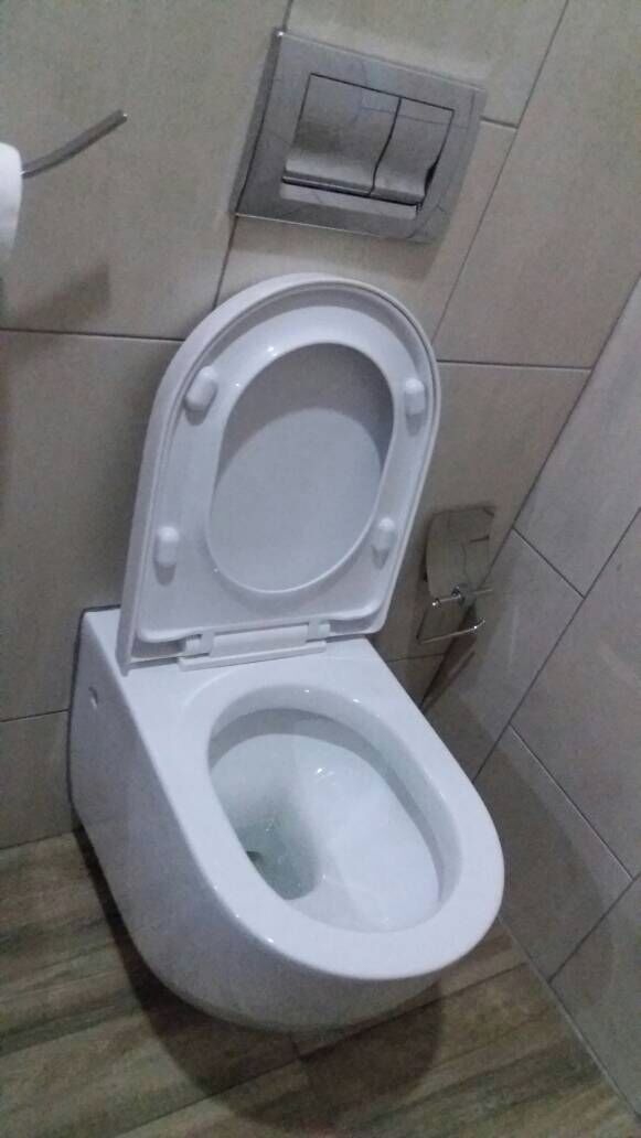 A standard white toilet with a flush handle and a flush button on the wall.