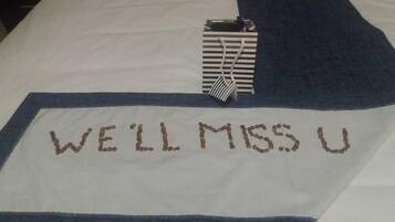 A bed with a blue and white blanket. The blanket has the text "WE'LL MISS U" embroidered in brown.