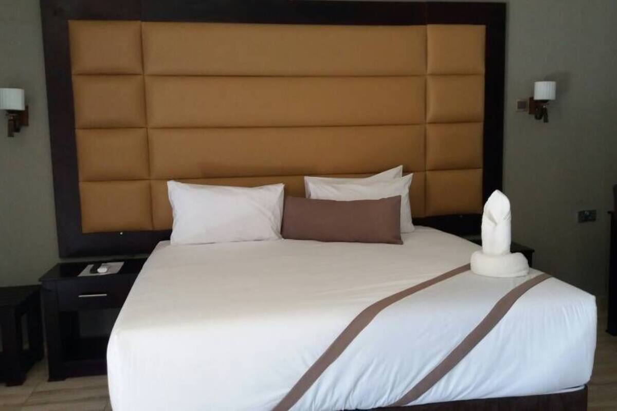 Una cama bien tendida con un cabecero grande, dos mesitas de noche y una silla.