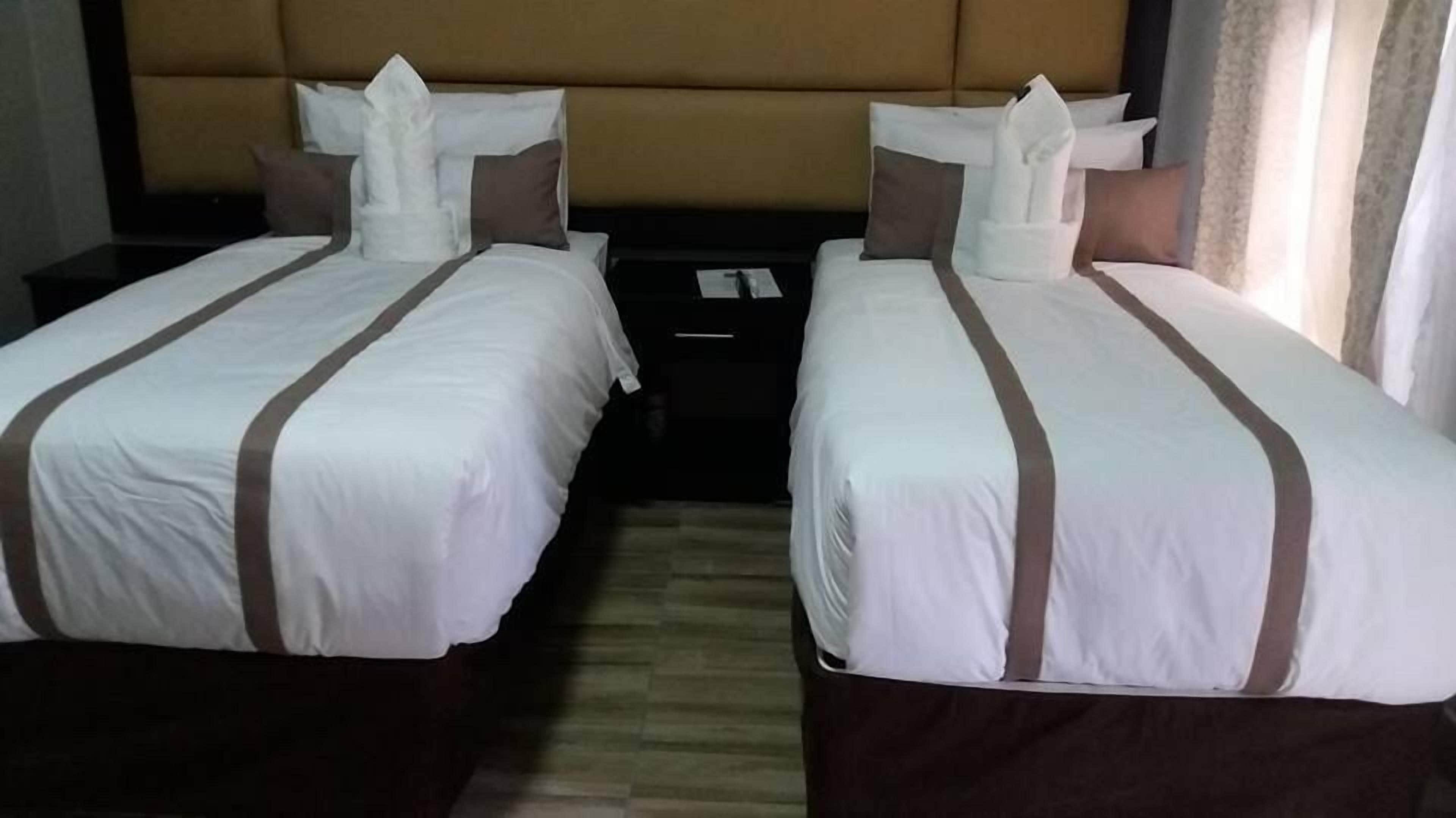 Une chambre d’hôtel avec deux lits simples, chacun doté d’une tête de lit, d’oreillers et d’une table de chevet placée entre les deux.