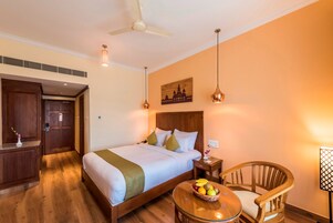 Habitación de hotel con cama, muebles de madera, una mesita con fruta y un ventilador de techo.