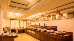 Un espace buffet doté d’un sol en marbre, d’un long comptoir où sont disposés des récipients contenant les aliments, et d’un éclairage suspendu.