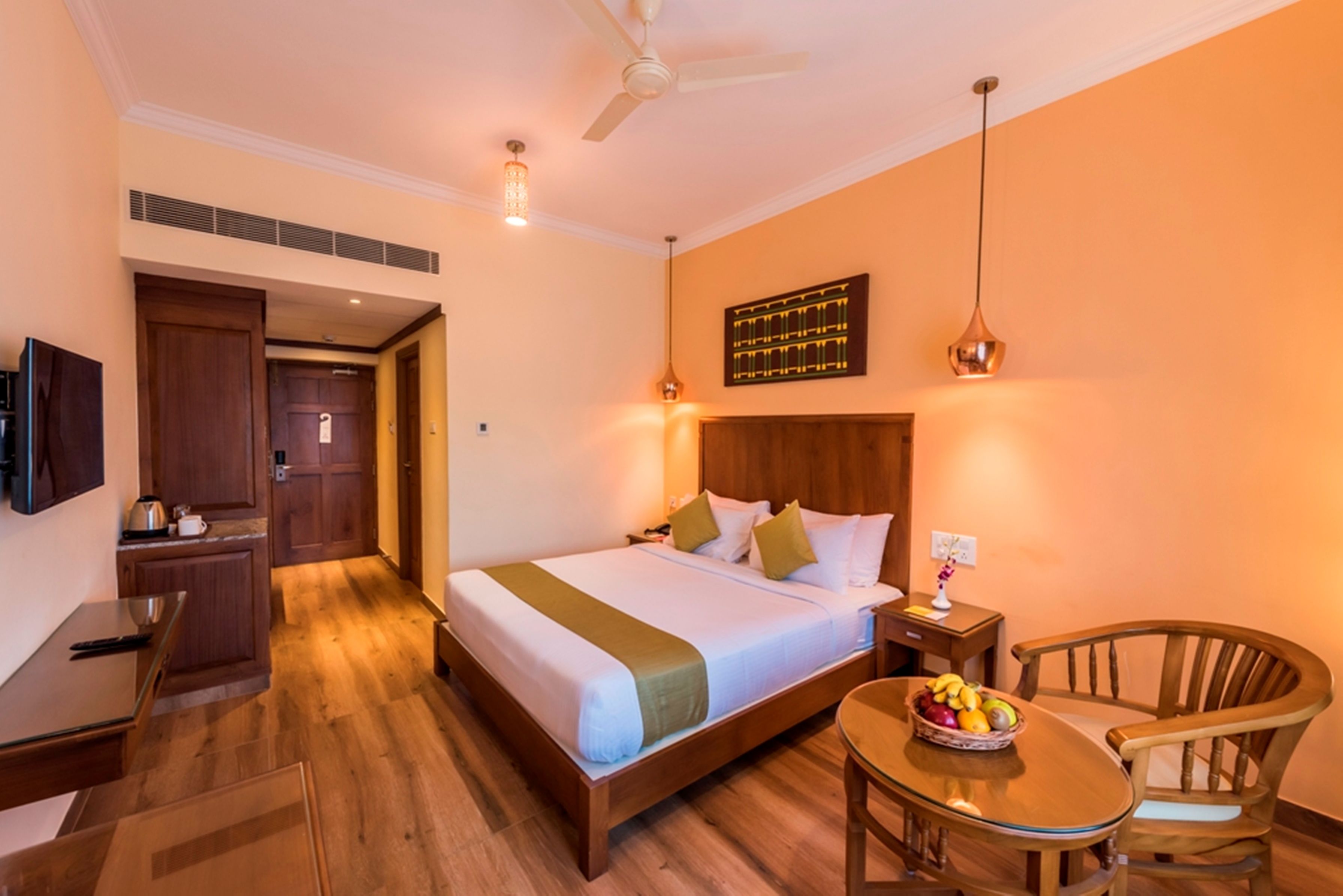A hotel room with a bed, bedside table, chair, and a small table with fruit.