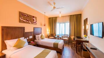 A hotel room with two beds, a desk, a chair, a TV, and a ceiling fan.