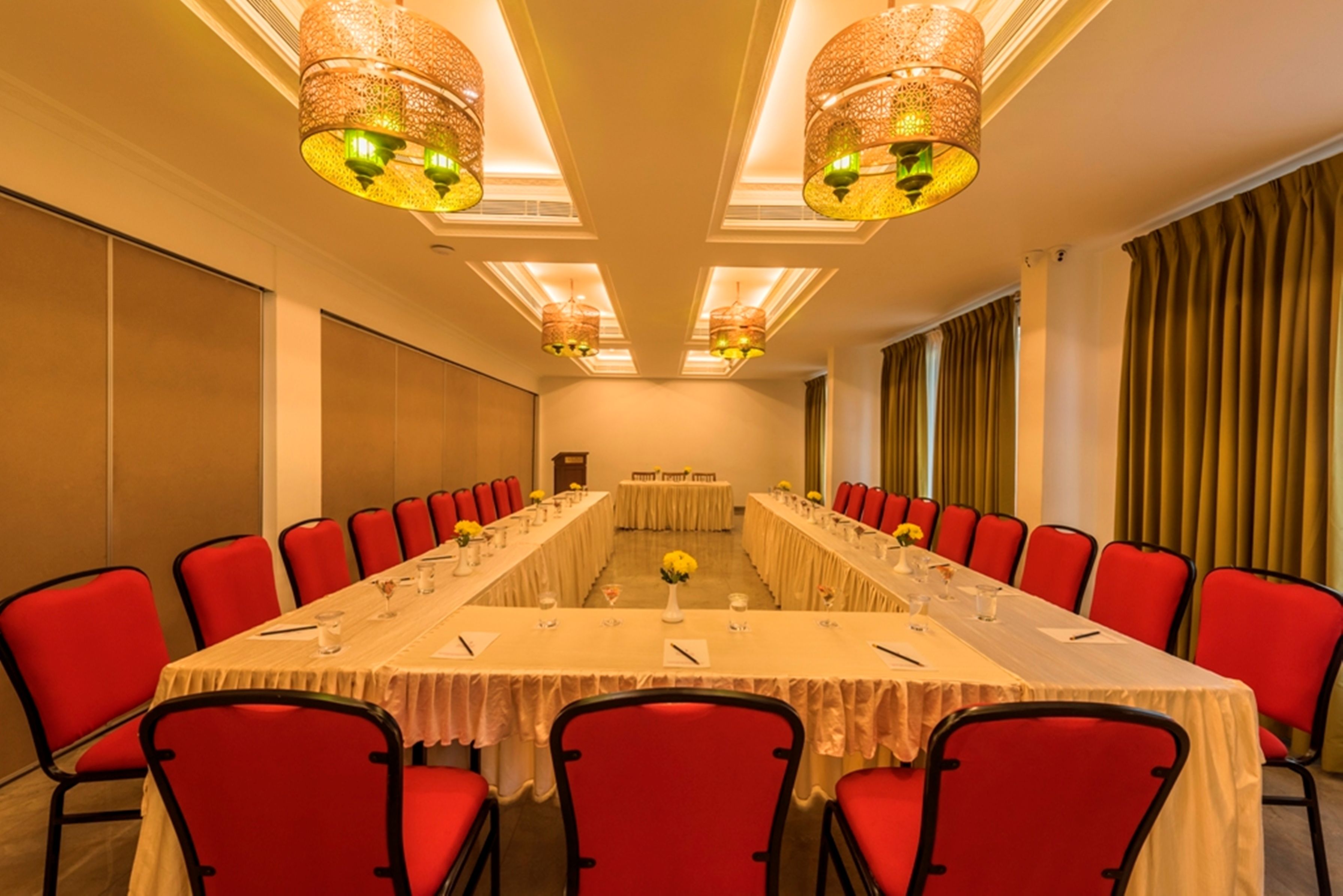 Una sala de conferencias con una mesa larga, sillas rojas y lámparas colgantes.
