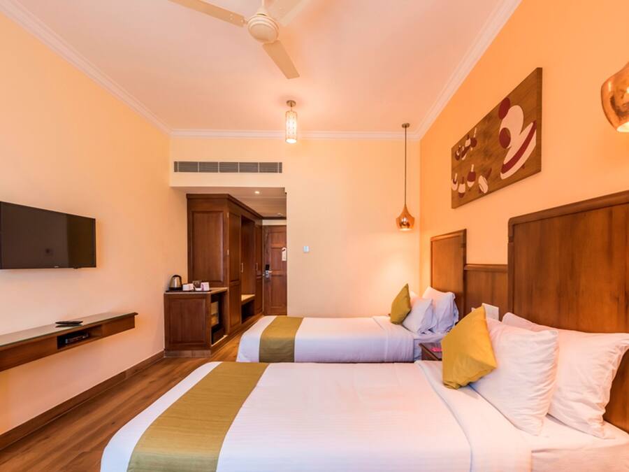 A hotel room with two beds, a TV, wooden furniture, and a painting on the wall.