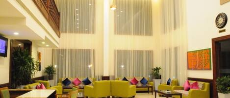 A spacious lobby with high ceilings, large windows with sheer curtains, and a variety of seating arrangements including sofas and chairs.