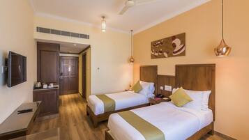 A hotel room with two beds, a desk, a television, and a ceiling fan.