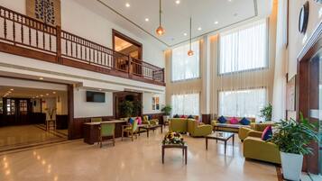 A spacious lobby with a high ceiling, a balcony, and large windows allowing natural light.