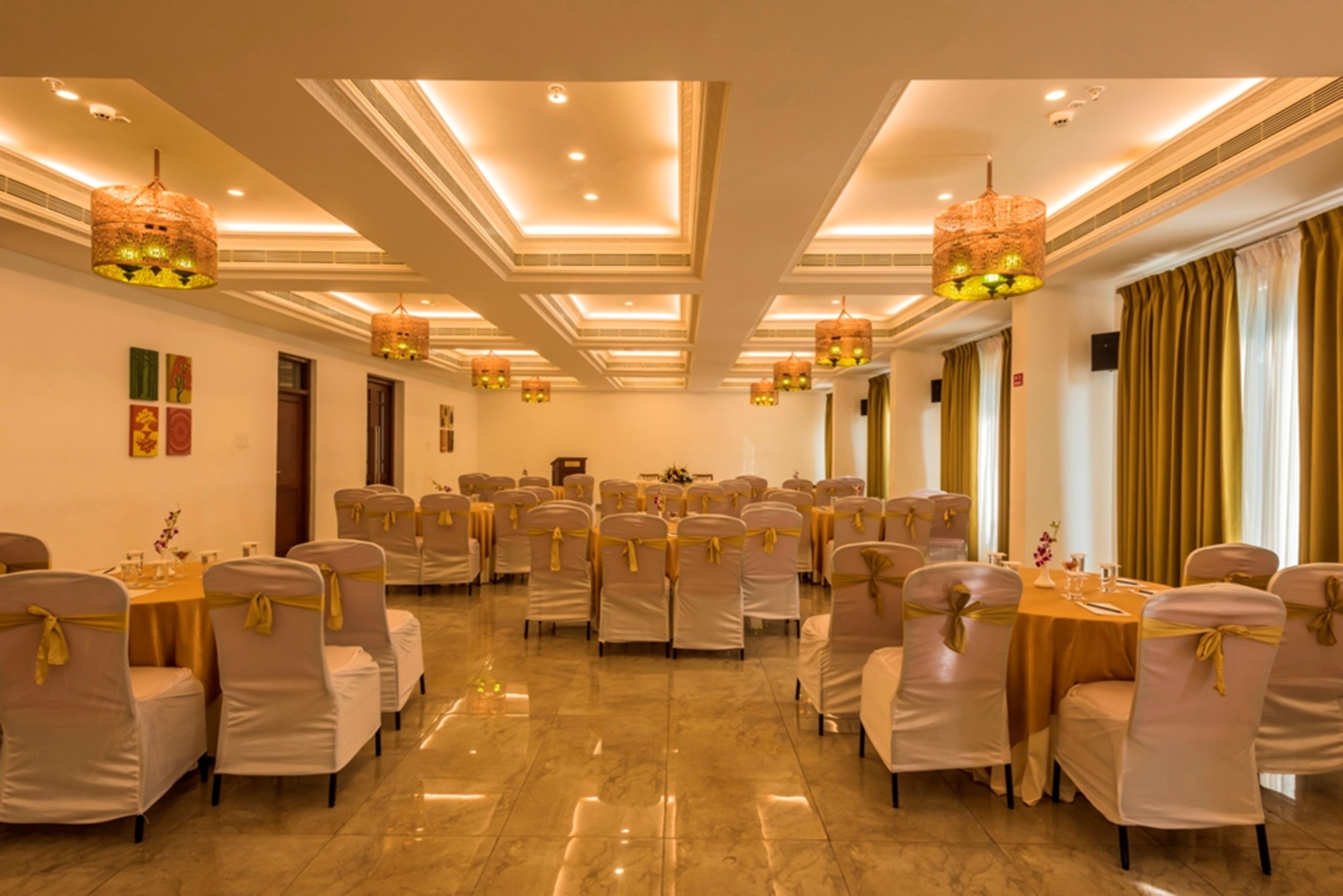 Un salón de banquetes con mesas redondas, sillas con cintas doradas y candelabros colgantes.