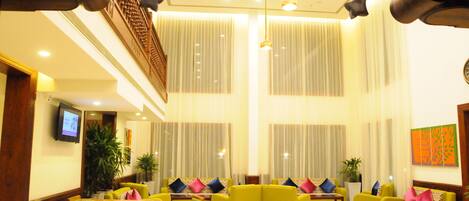 A lobby with yellow sofas, a wooden reception desk, and a television screen.