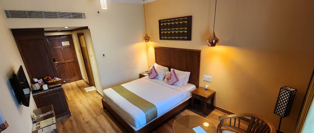 A hotel room with a bed, bedside table, chair, and a desk with a chair.