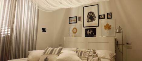 Una cama bien hecha con almohadas y una colcha, una lámpara de noche y una pared con cuadros enmarcados.