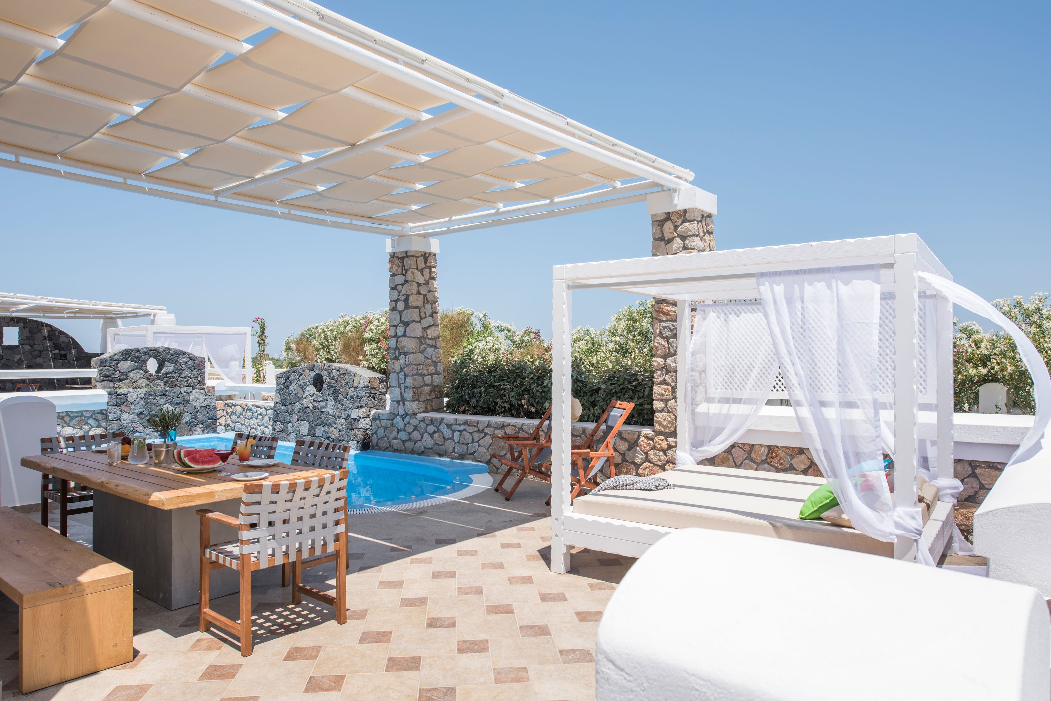 An outdoor pool area with a pergola, stone walls, and a canopy bed.