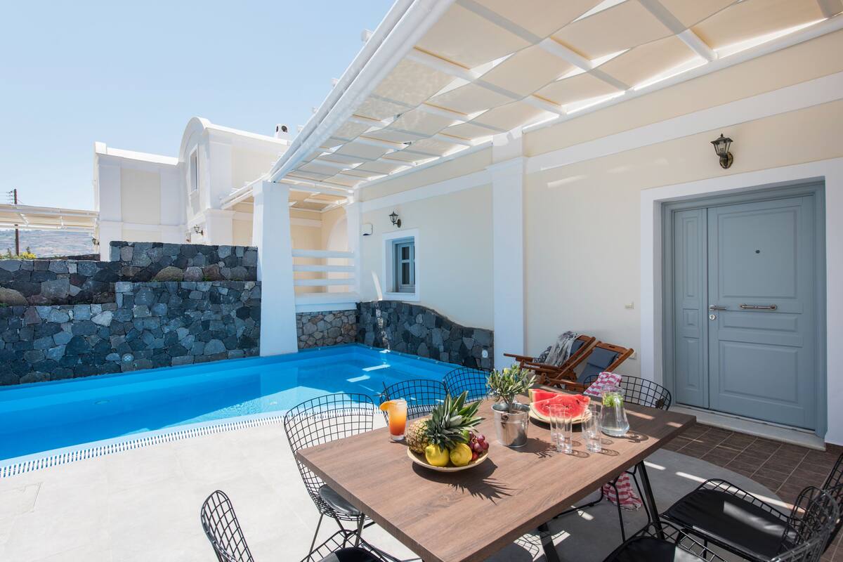 A poolside dining area with a table set for two, a stone wall, and a pool.