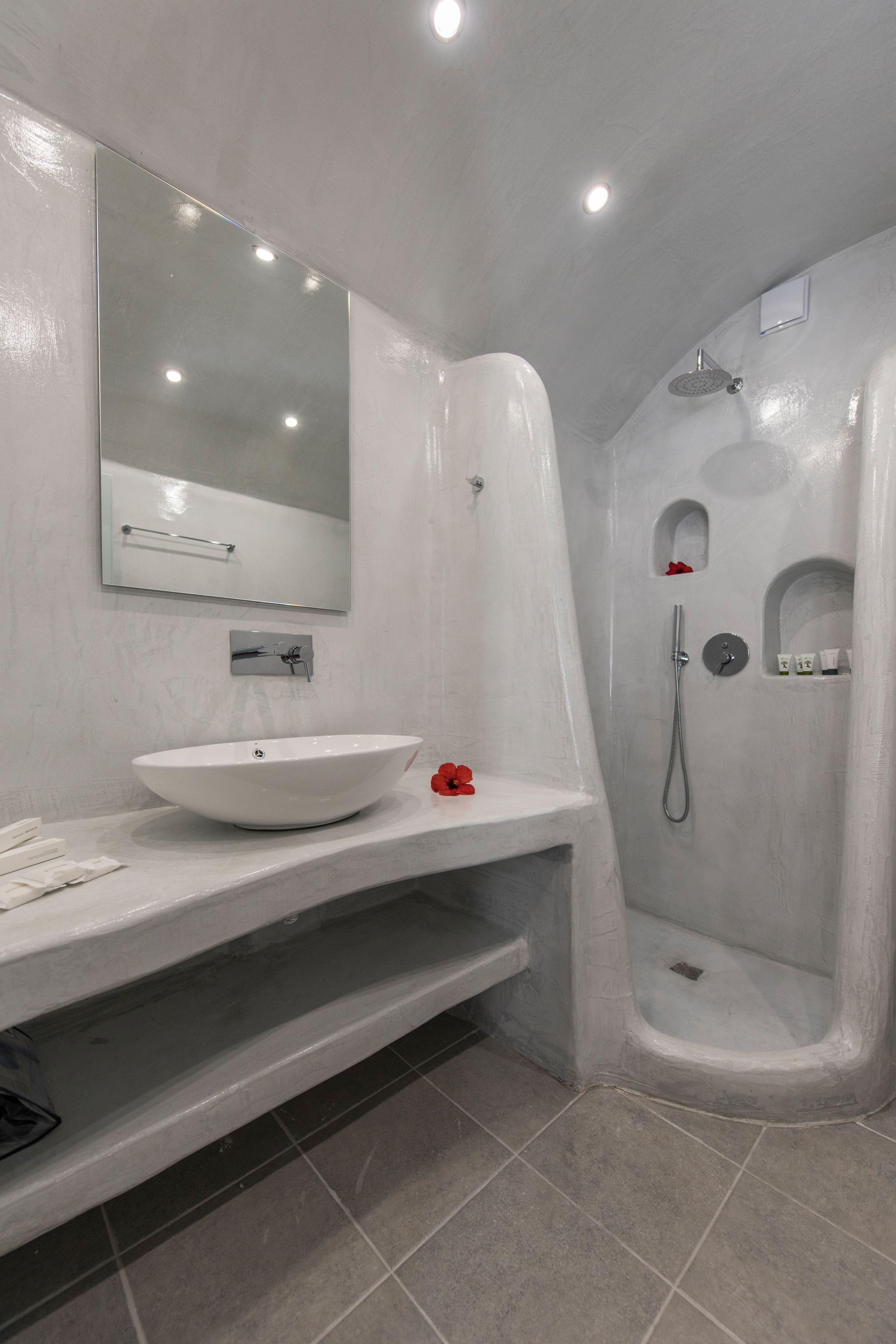A modern bathroom with a large white sink, a mirror, and a shower area.