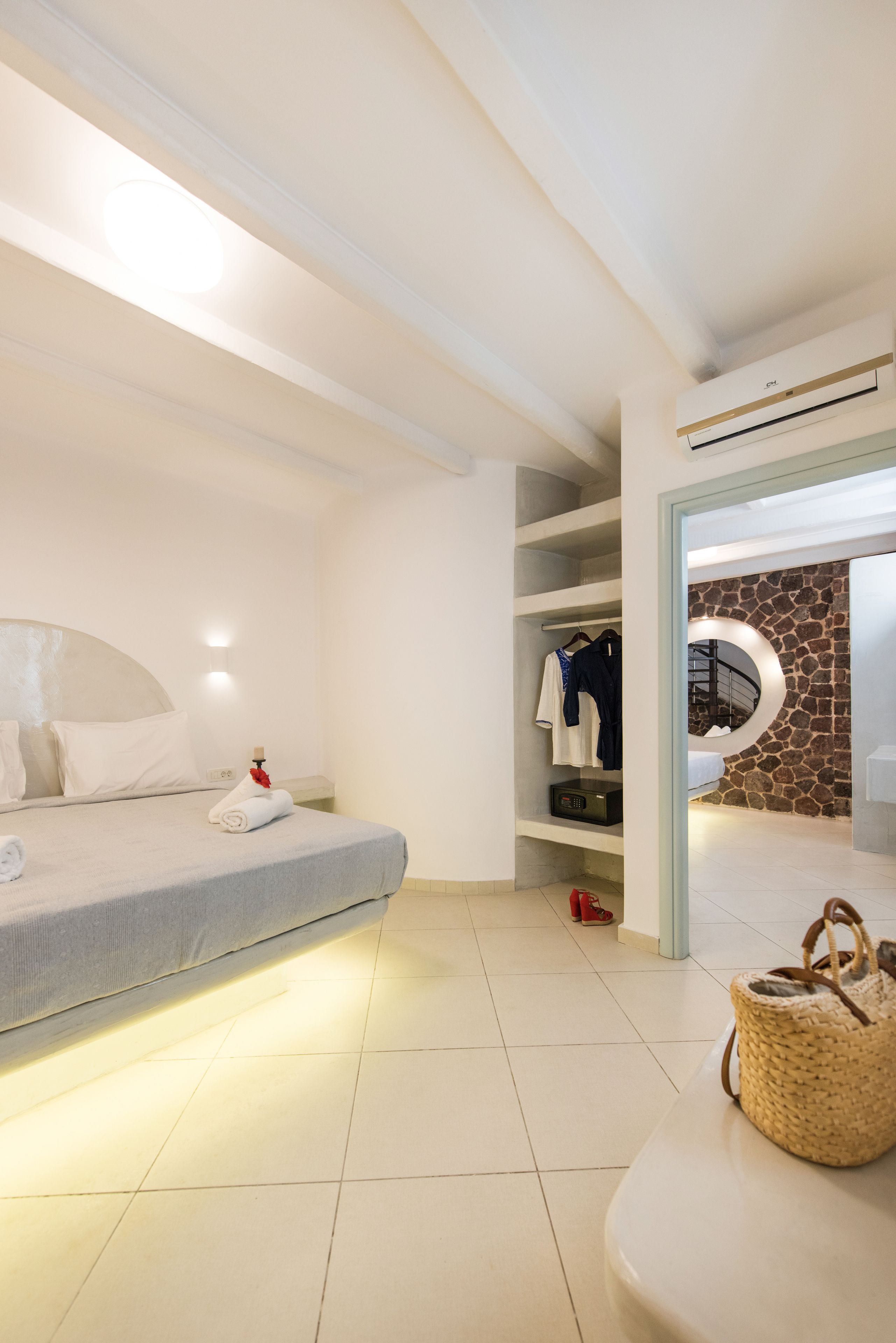 Ein modernes Schlafzimmer mit Bett, Nachttisch, Wand-Klimaanlage, Kleiderschrank und einer runden Steinwand.