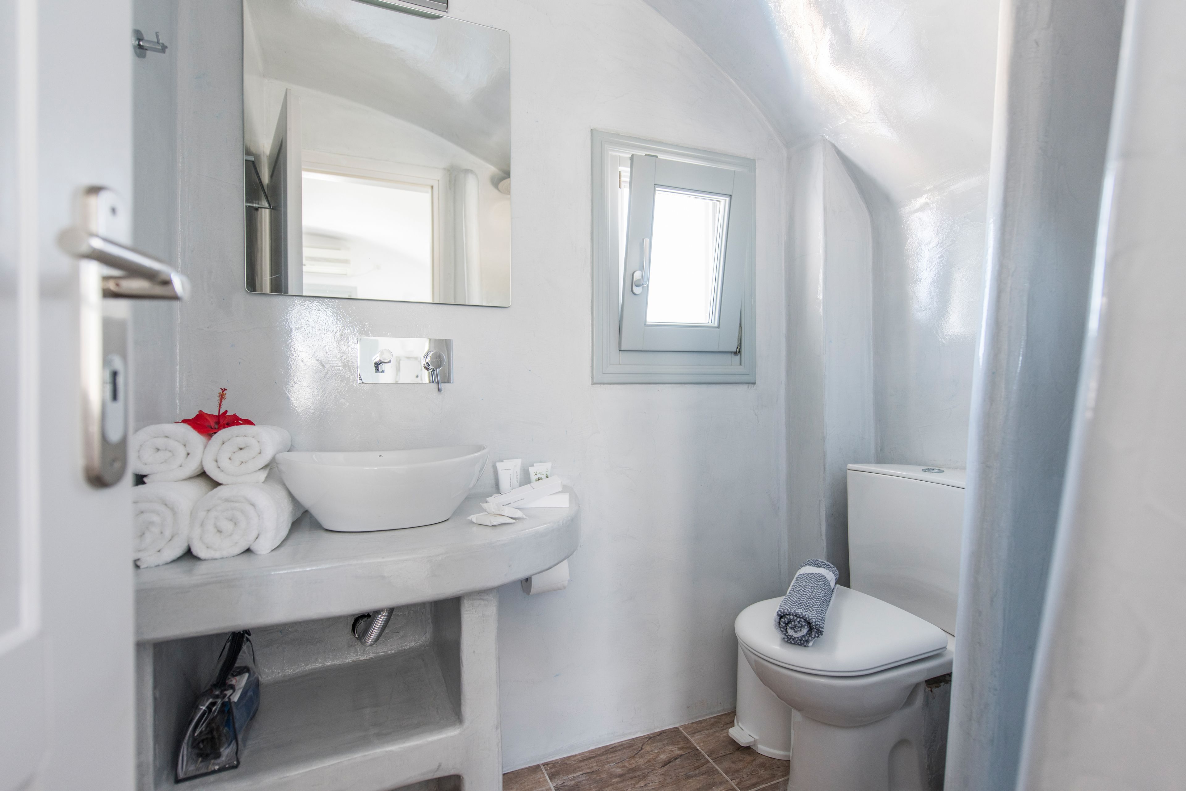 A bathroom with a white sink, mirror, and toilet. There are towels and toiletries on the sink.