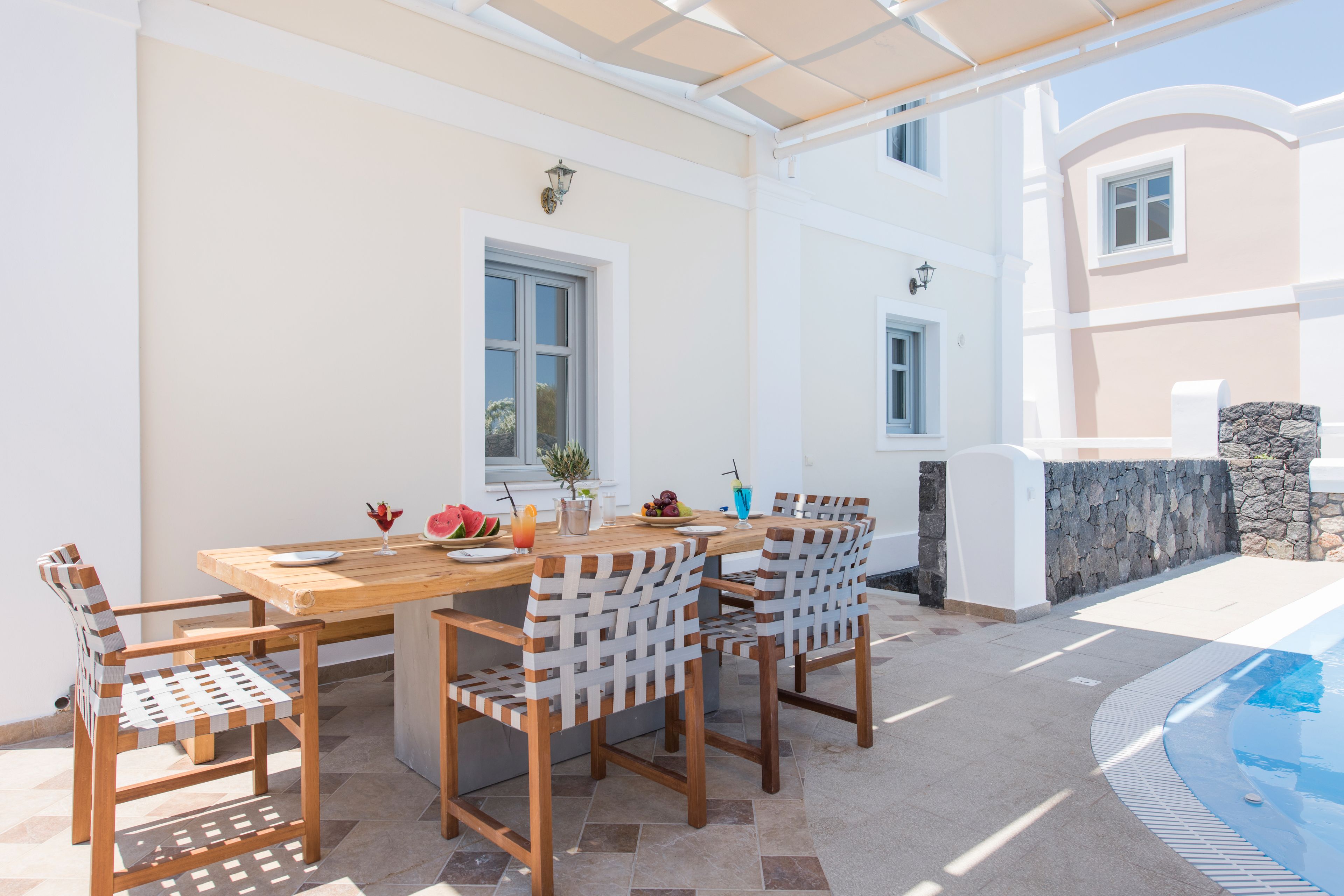 A wooden table with chairs, a pool, and a stone wall.
