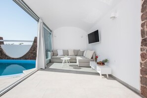 Una sala de estar moderna con sofá, mesa de centro y televisor, con vista a una piscina.