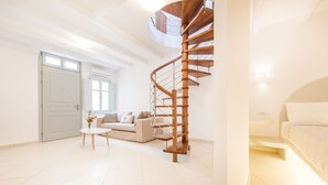 A spacious living area with a wooden spiral staircase, a sofa set, and a small table with flowers. - Secret Earth Santorini (Santorini)