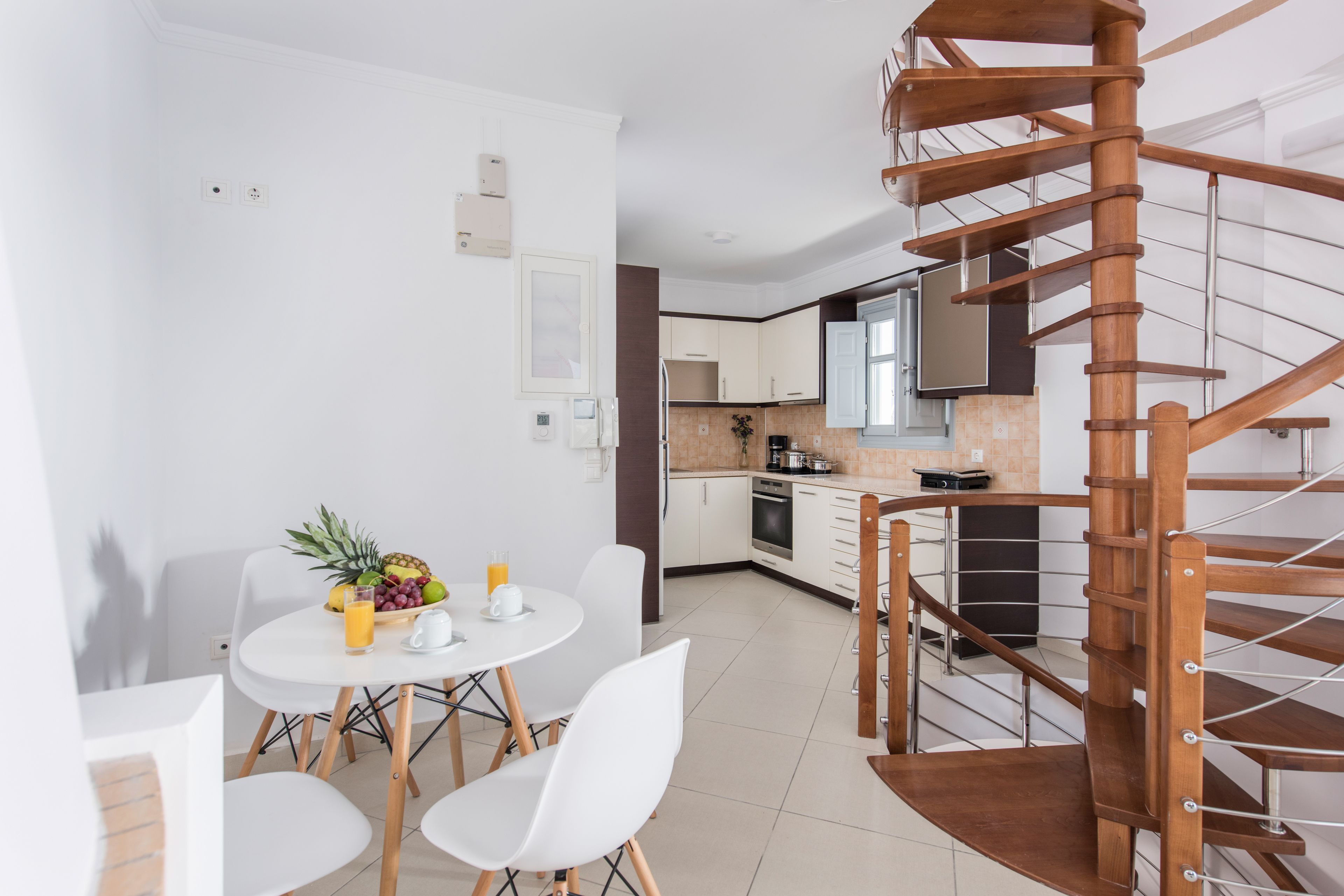 Una cocina moderna con armarios blancos, una escalera espiral de madera y un comedor con una mesa redonda y sillas blancas.