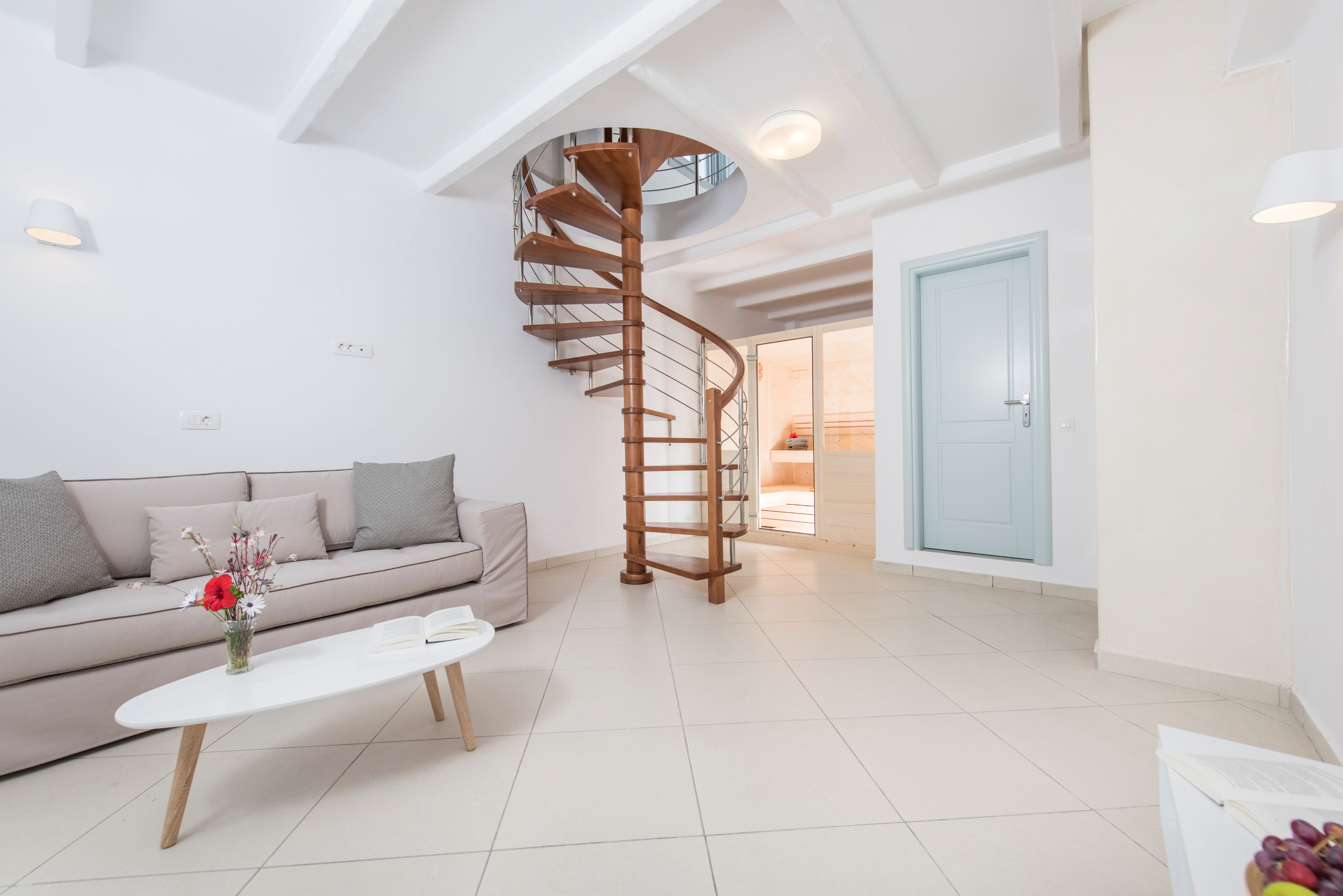A modern living room with a spiral staircase, a sofa, a coffee table, and a door leading to another room.