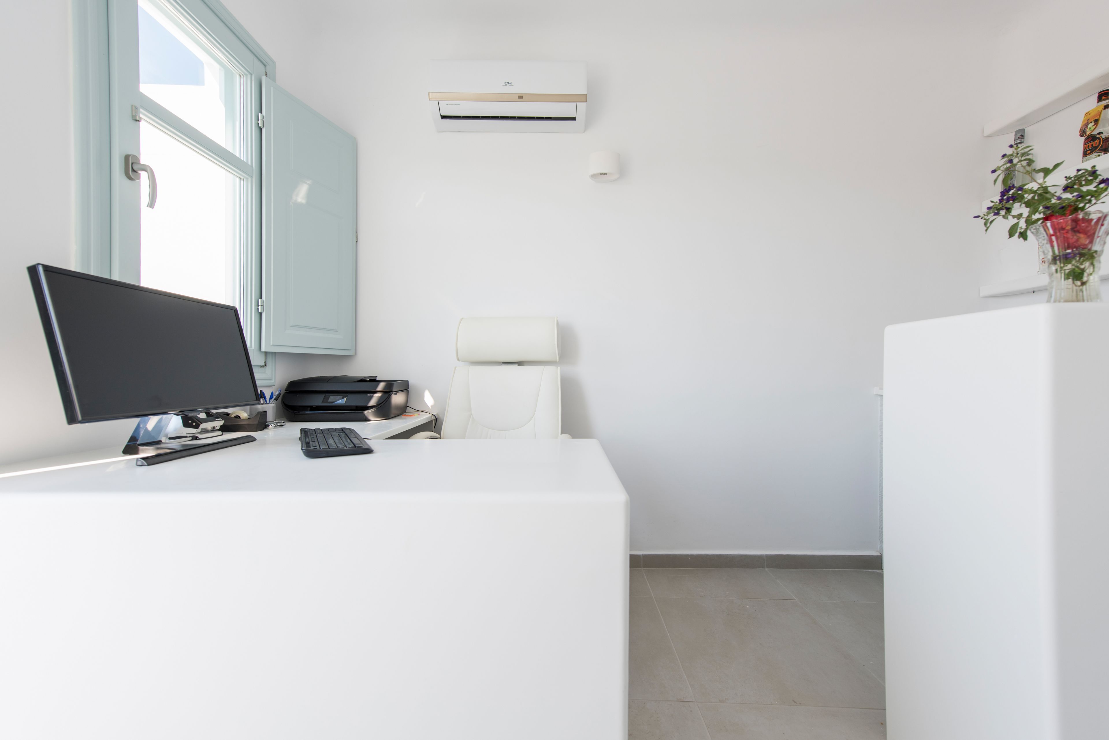 Un espacio de oficina moderno y minimalista con escritorio blanco, computadora, teclado e impresora.