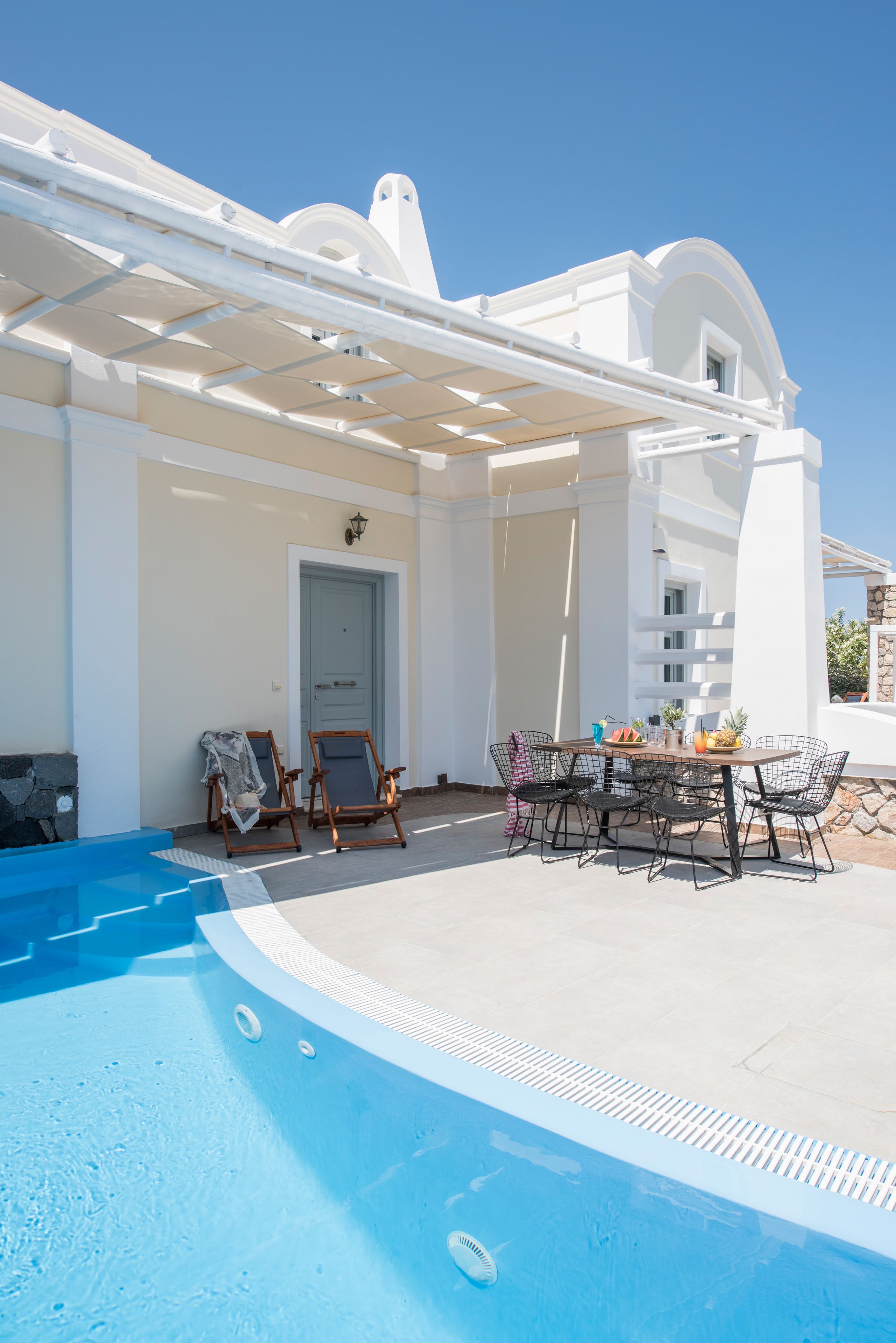 A poolside area with a white building, a pool, and outdoor furniture.