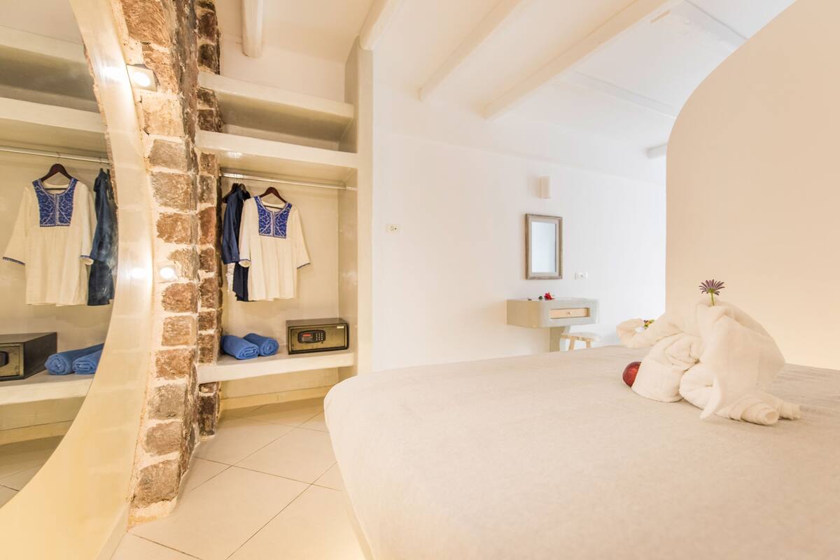 A hotel room with a stone wall, a bed, a wardrobe, and a mirror.