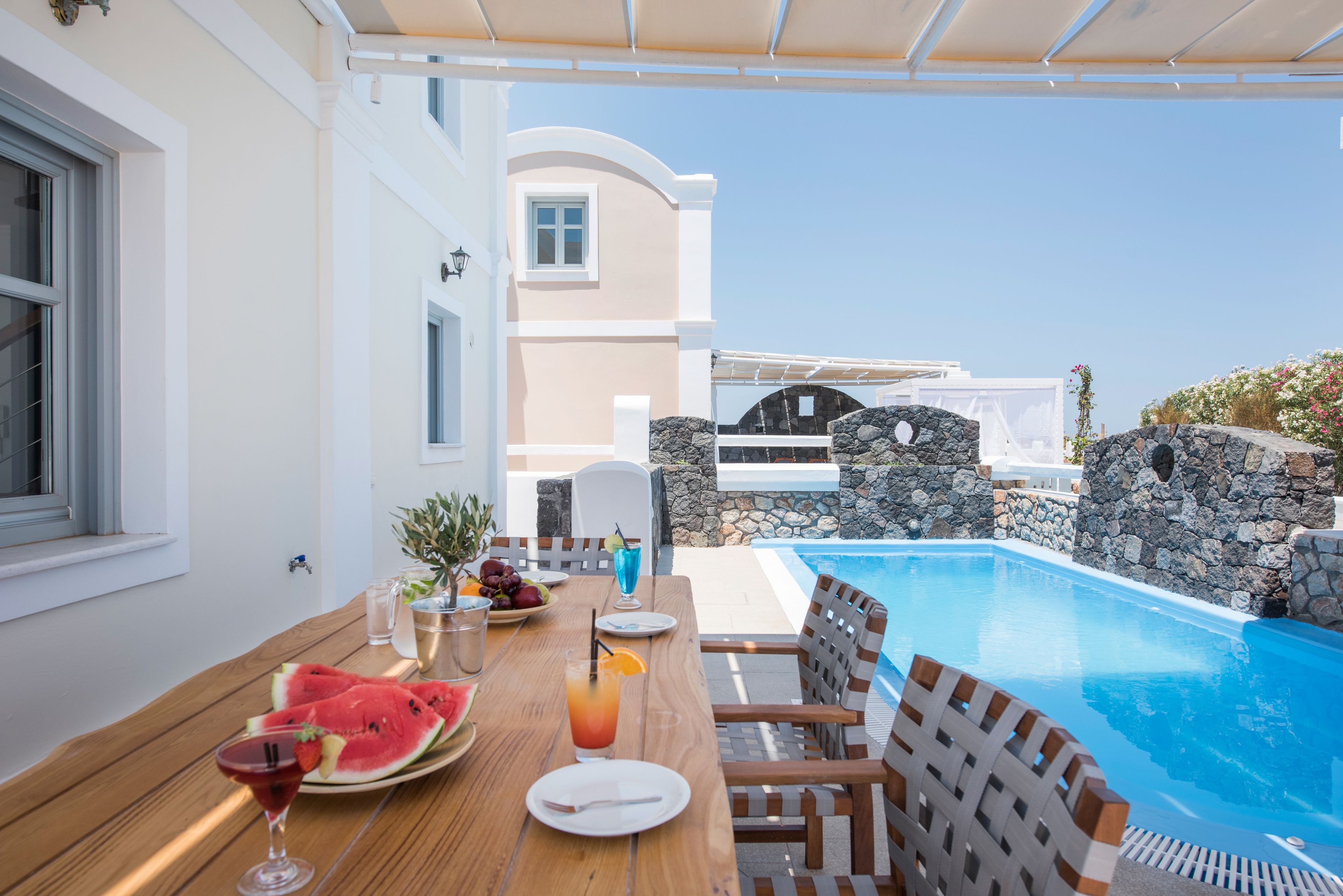A poolside dining area with a wooden table, chairs, and a view of a swimming pool.
