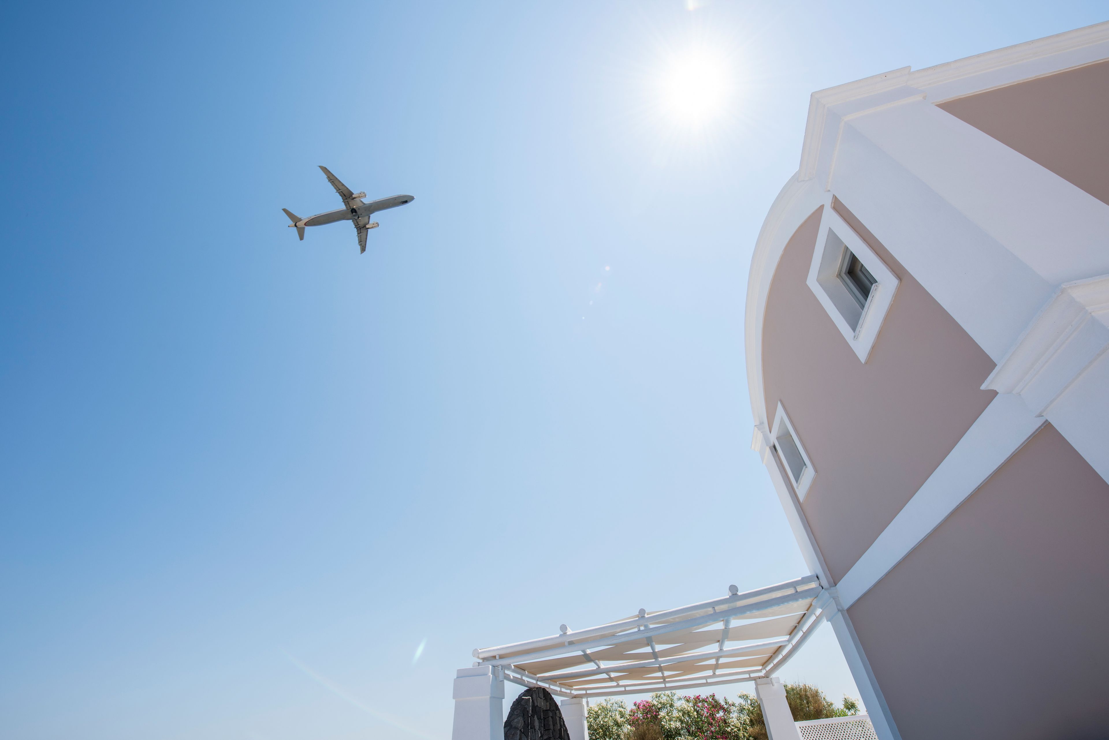 Klarer Himmel mit einem vorbeifliegenden Flugzeug und einem Gebäude mit weißer Fassade und einem Fenster.