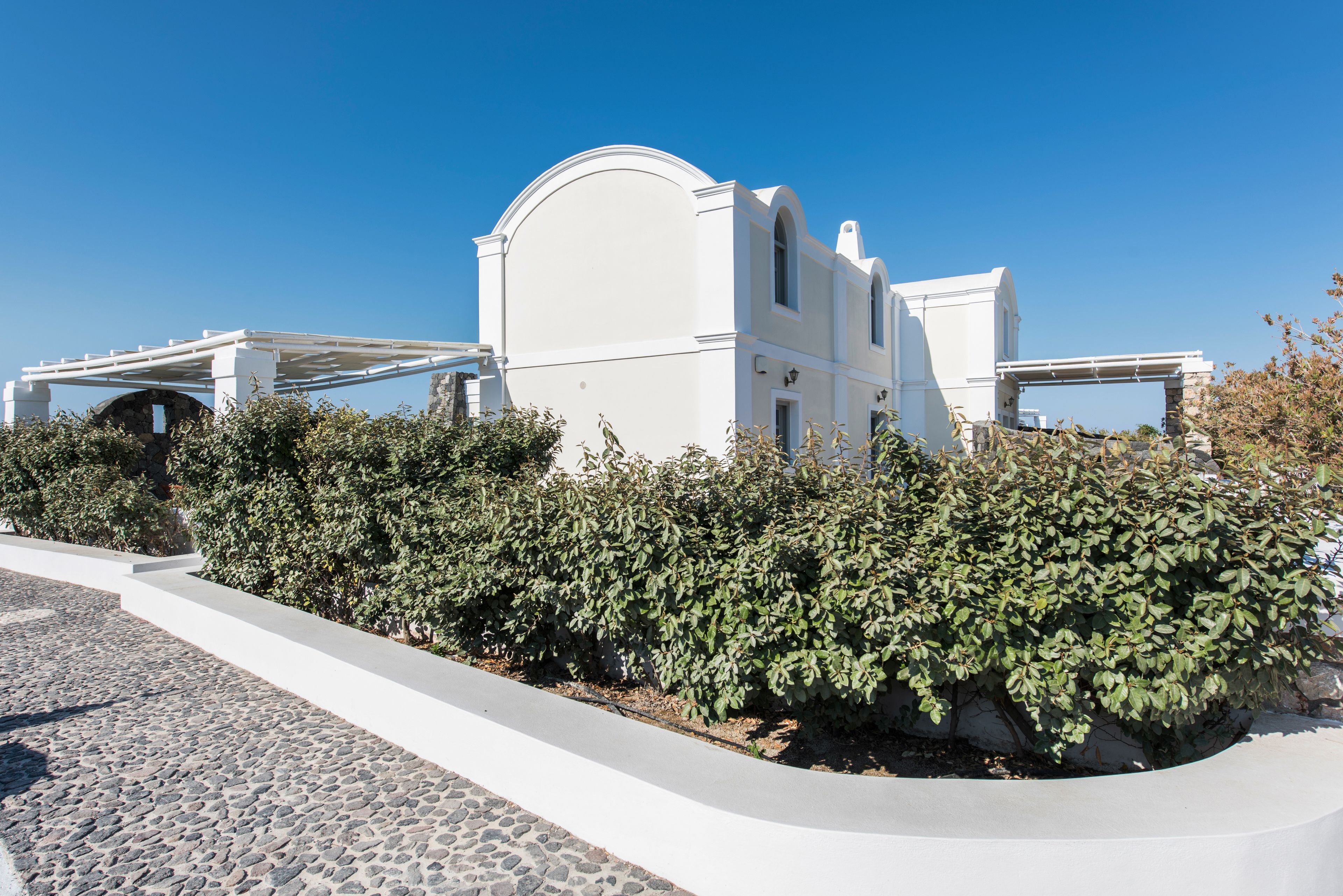 Un edificio blanco con fachada curva y ventanas arqueadas, rodeado de follaje y un camino empedrado.