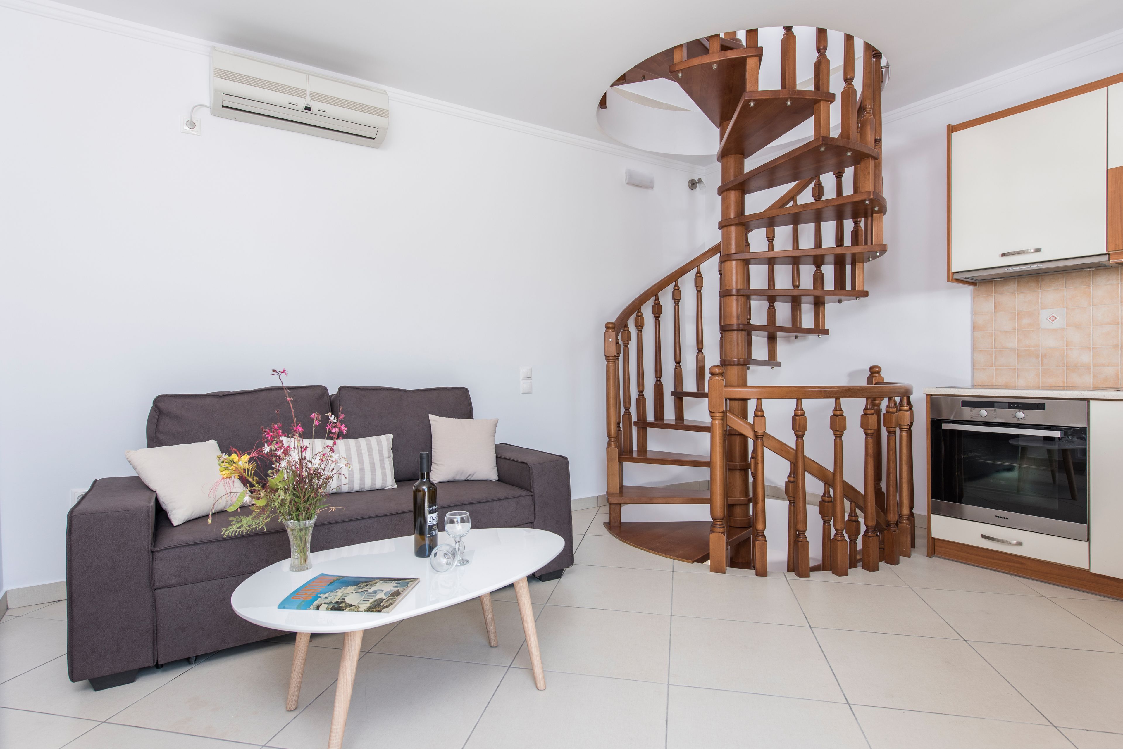 A modern living room with a grey sofa, white coffee table, and a wooden spiral staircase.