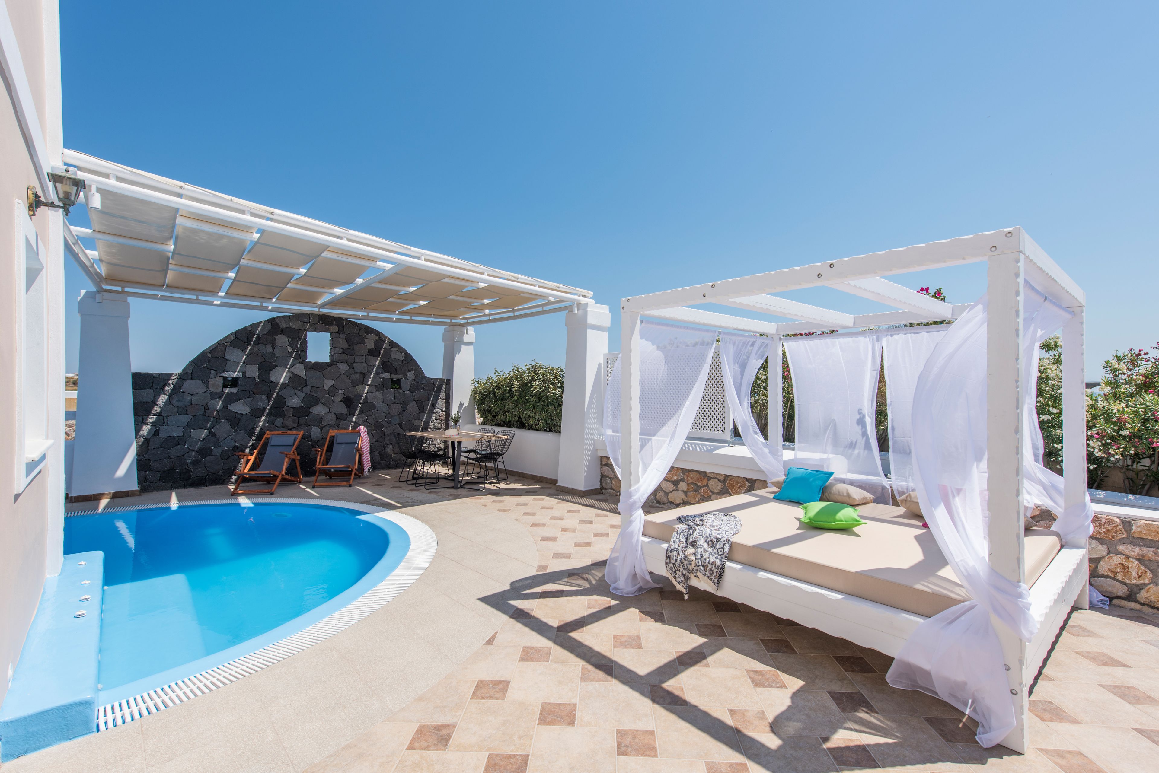 A poolside area with a white pergola, a stone wall, and a bed with a canopy.