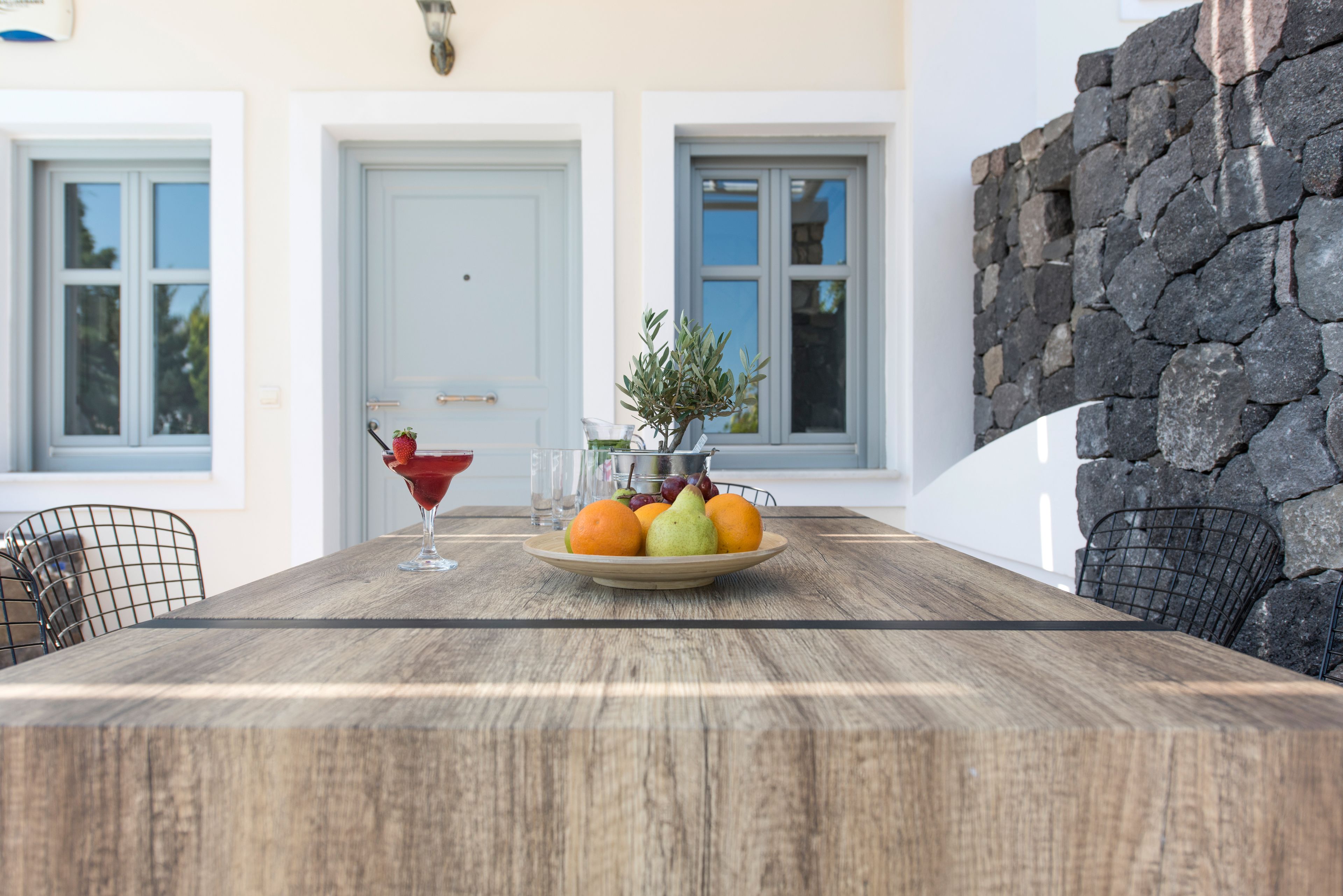 Uma mesa de madeira com uma tigela de frutas, uma taça de martini e um vaso com folhagem.