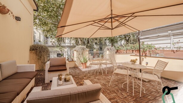 A cozy outdoor seating area with wicker furniture, a large umbrella, and potted plants. - Residenza Scarlatti (Naples)