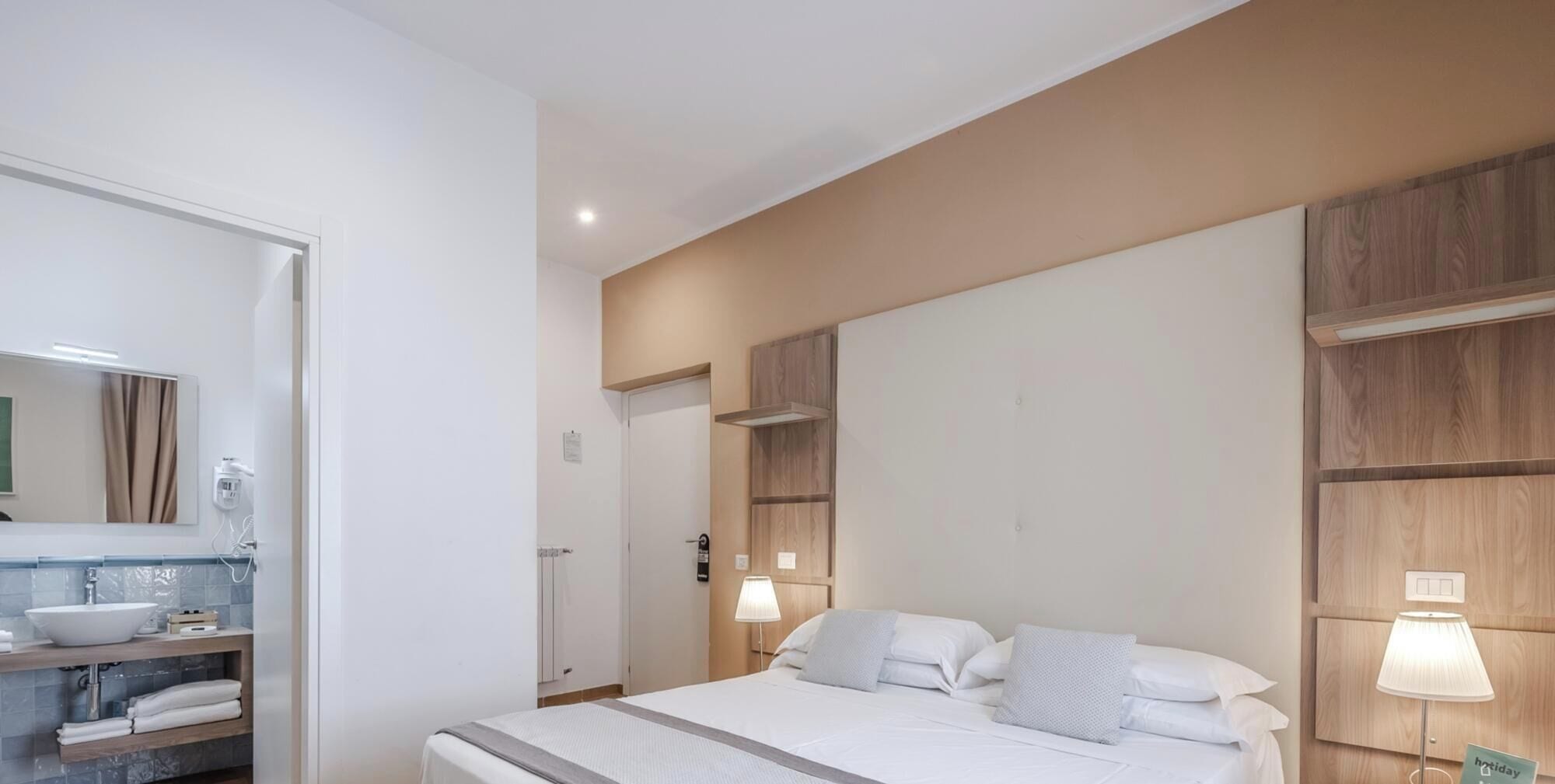 Ein Hotelzimmer mit Bett, Nachttischlampen, einem Badezimmer mit Waschbecken und Spiegel sowie Holzvertäfelung an den Wänden.