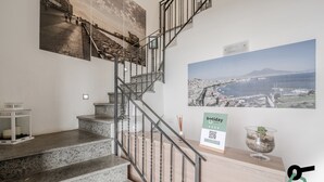 A staircase with granite steps and metal railings, leading to a landing with a view of a coastal cityscape. - Residenza Scarlatti (Naples)
