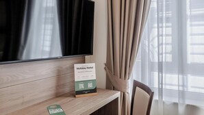 A hotel room with a flat-screen TV mounted on a wooden wall, a desk with a sign, and a chair. - Residenza Scarlatti (Naples)