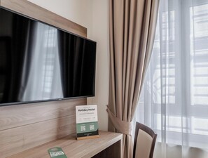 A hotel room with a flat-screen TV mounted on a wooden wall, a desk with a sign, and a chair. - Residenza Scarlatti (Naples)